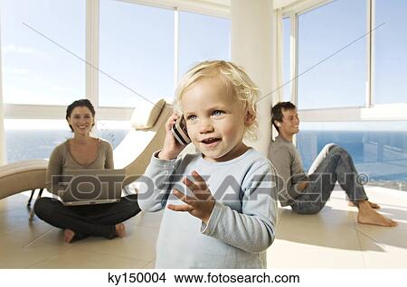 Picture - Little girl using mobile phone, parents in background. Fotosearch