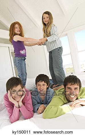 Smiling couple and three children on bed View Large Photo Image Stock Image - Smiling couple and three children on bed. Fotosearch
