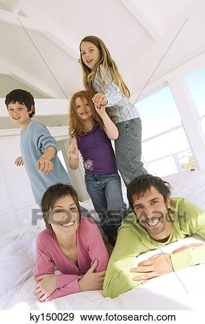 Smiling couple and three children on bed View Large Photo Image Stock Photo - Smiling couple and three children on bed. Fotosearch