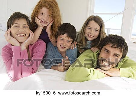 Smiling couple with 3 children lying on bed View Large Photo Image Stock Photograph - Smiling couple with 3 children lying on bed. Fotosearch
