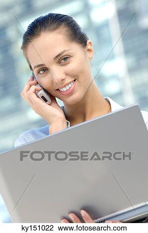 Businesswoman using mobile phone with laptop in hand, smiling View Large Photo Image Stock Image - Businesswoman using mobile phone with laptop in hand, smiling. Fotosearch