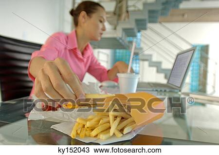 Businesswoman eating French fries, using laptop View Large Photo Image Stock Image - Businesswoman eating French fries, using laptop. Fotosearch