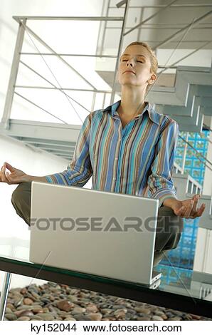 Picture - Young businesswoman meditating on tabletop in office. Fotosearch