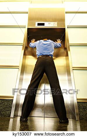 Stock Photo - Businessman standing in front of closed door of elevator, low angle view. Fotosearch
