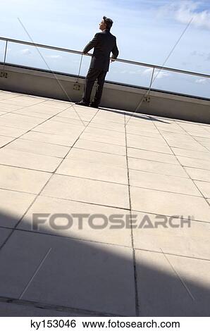 Stock Photograph - Businessman standing on terrace, rear view. Fotosearch