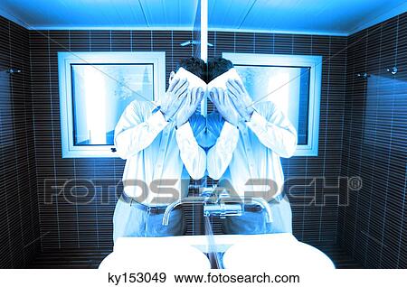 Stock Photo - Man covering face while leaning by mirror in washroom. Fotosearch