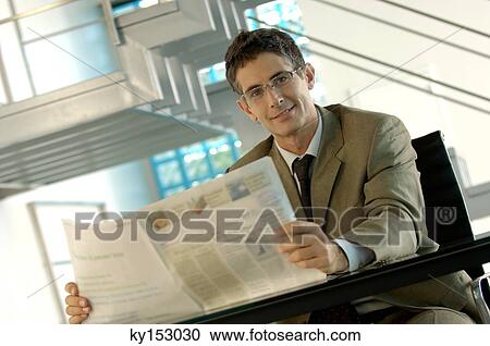 Stock Image - Mid adult businessman holding newspaper, portrait. Fotosearch