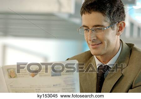 Stock Photography - Mid adult businessman reading newspaper at office, smiling. Fotosearch