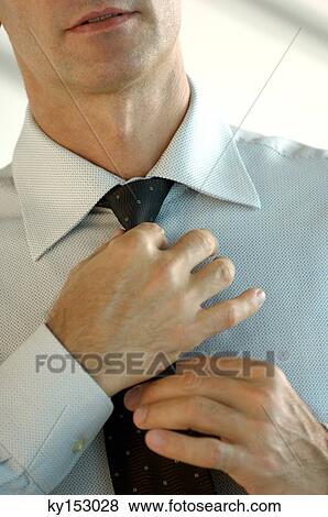 Stock Photo - Young businessman adjusting tie, close-up. Fotosearch