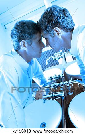 Young businessman looking at mirror in washroom View Large Photo Image Stock Image - Young businessman looking at mirror in washroom. Fotosearch