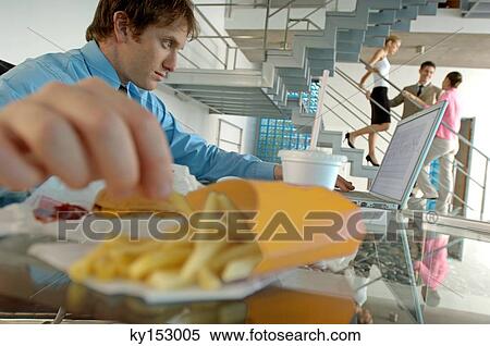Young businessman using laptop and eating French fries View Large Photo Image Stock Photography - Young businessman using laptop and eating French fries. Fotosearch