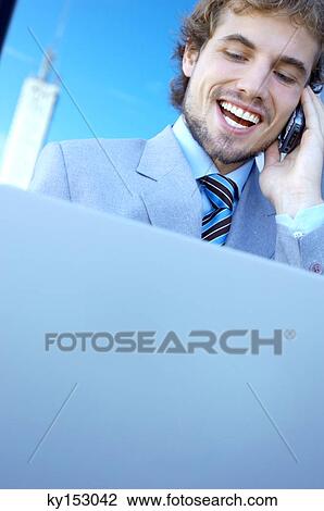 Young businessman using mobile phone and laptop, smiling View Large Photo Image Stock Image - Young businessman using mobile phone and laptop, smiling. Fotosearch
