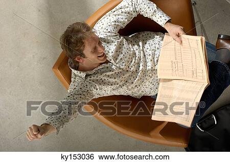 Young man reading newspaper, high angle view View Large Photo Image Stock Photograph - Young man reading newspaper, high angle view. Fotosearch