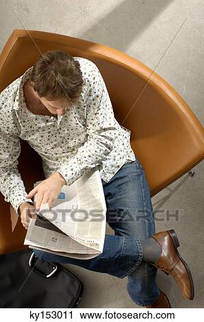 Young man sitting on chair and reading newspaper, overhead view View Large Photo Image Stock Image - Young man sitting on chair and reading newspaper, overhead view. Fotosearch