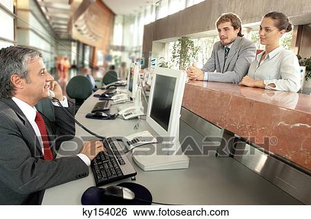 Stock Photograph - Businessman using telephone with colleagues leaning on counter. Fotosearch
