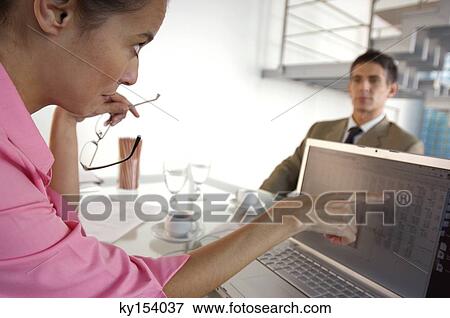 Businesswoman checking in laptop with businessman sitting in background View Large Photo Image Stock Photo - Businesswoman checking in laptop with businessman sitting in background. Fotosearch