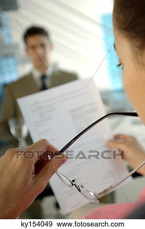 Stock Photo - Businesswoman reading paper with colleague in background. Fotosearch