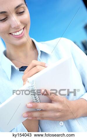 Stock Image - Businesswoman writing on notebook, smiling. Fotosearch