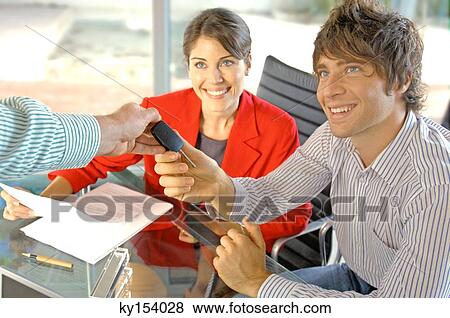Stock Photo - Car dealer handing car key to customer, smiling. Fotosearch