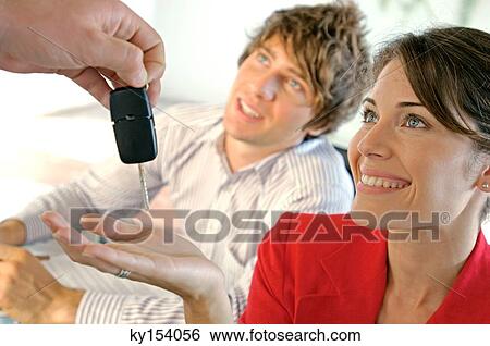 Stock Photograph - Car dealer handing car key to customer, smiling. Fotosearch