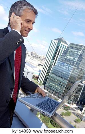 Mature man using mobile phone and laptop in balcony View Large Photo Image Stock Photo - Mature man using mobile phone and laptop in balcony. Fotosearch