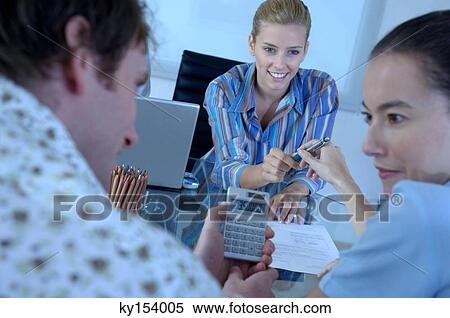 Stock Photography - Two businesswomen and businessman in office, man using calculator. Fotosearch