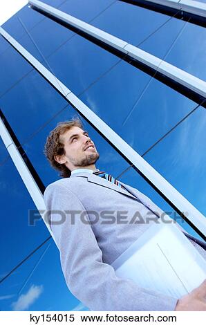 Young businessman holding file by office building, low angle view View Large Photo Image Stock Photography - Young businessman holding file by office building, low angle view. Fotosearch