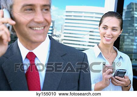 Stock Image - Business people using mobile phone, smiling. Fotosearch