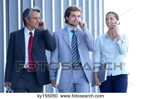 Stock Image - Business people using mobile phone, smiling. Fotosearch