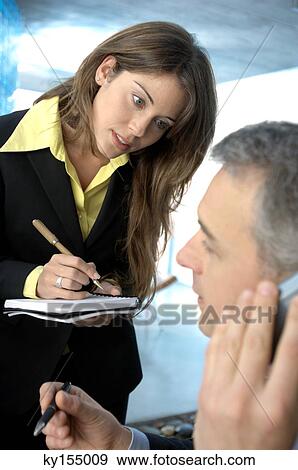 Mature businessman using mobile phone while young woman writing View Large Photo Image Stock Photo - Mature businessman using mobile phone while young woman writing. Fotosearch