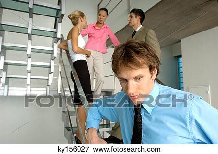 Businessman standing by staircase with colleagues in background View Large Photo Image Stock Photo - Businessman standing by staircase with colleagues in background. Fotosearch