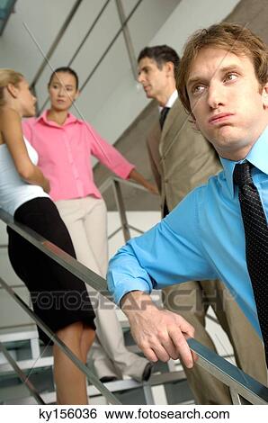 Businessman standing by staircase with colleagues in background View Large Photo Image Stock Photograph - Businessman standing by staircase with colleagues in background. Fotosearch