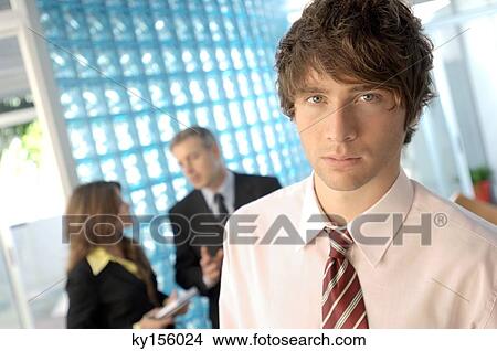 Businessman standing in office with colleagues in background View Large Photo Image Picture - Businessman standing in office with colleagues in background. Fotosearch