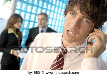 Businessman using mobile phone with colleagues in background View Large Photo Image Stock Image - Businessman using mobile phone with colleagues in background. Fotosearch