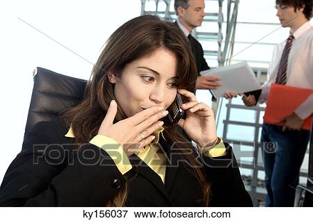 Businesswoman using mobile phone with colleagues standing in background View Large Photo Image Stock Photo - Businesswoman using mobile phone with colleagues standing in background. Fotosearch