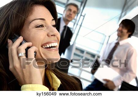 Stock Photo - Businesswoman using mobile phone with colleagues in background. Fotosearch