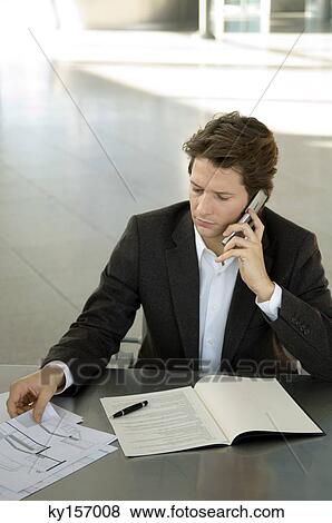 Stock Photo - Businessman talking on a mobile phone at a desk. Fotosearch