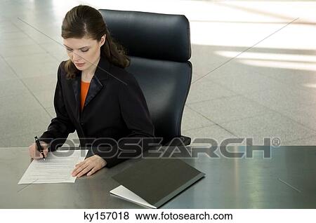 Businesswoman sitting at a desk and signing documents View Large Photo Image Stock Photo - Businesswoman sitting at a desk and signing documents. Fotosearch