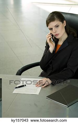 Stock Image - Businesswoman talking on a mobile phone in an office. Fotosearch
