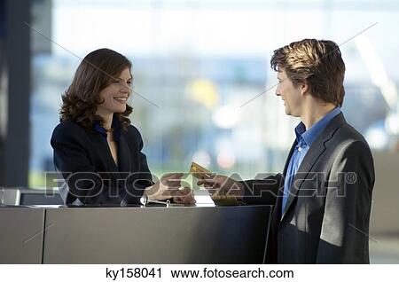 Stock Image - Businessman giving a credit card to a hotel receptionist. Fotosearch