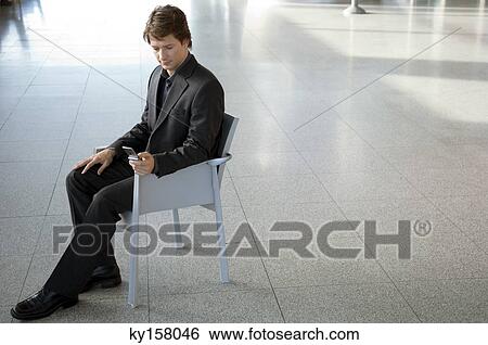 Businessman sitting in an armchair and text messaging with a mobile phone View Large Photo Image Stock Photograph - Businessman sitting in an armchair and text messaging with a mobile phone. Fotosearch