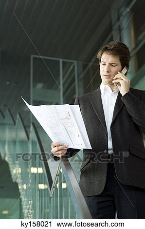 Businessman talking on a mobile phone and looking at a blueprint View Large Photo Image Stock Image - Businessman talking on a mobile phone and looking at a blueprint. Fotosearch