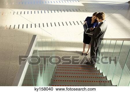 Stock Image - High angle view of a businessman and a businesswoman using a laptop. Fotosearch