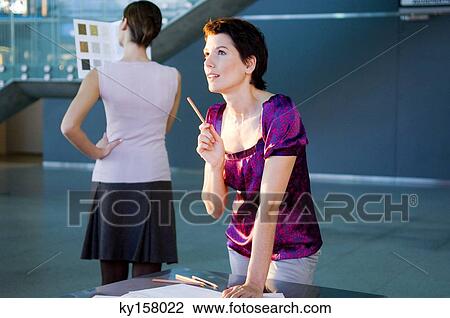 Mid adult woman making a blueprint with a young woman looking at a color swatch View Large Photo Image Stock Image - Mid adult woman making a blueprint with a young woman looking at a color swatch. Fotosearch