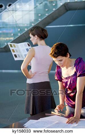 Mid adult woman making a blueprint with a young woman looking at a color swatch View Large Photo Image Stock Image - Mid adult woman making a blueprint with a young woman looking at a color swatch. Fotosearch