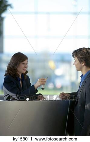 Stock Image - Receptionist giving the key of a hotel room to a businessman. Fotosearch