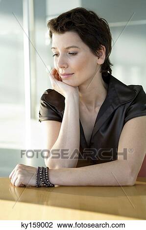 Close-up of a mid adult woman sitting at a table with her hand on her chin View Large Photo Image Stock Image - Close-up of a mid adult woman sitting at a table with her hand on her chin. Fotosearch