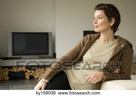 Stock Photo - Mid adult woman leaning against a couch. Fotosearch