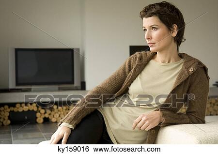 Mid adult woman leaning against a couch View Large Photo Image Stock Photograph - Mid adult woman leaning against a couch. Fotosearch
