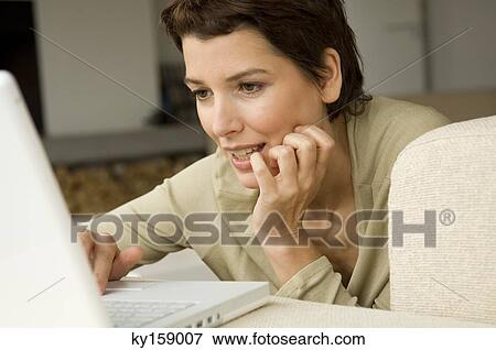 Mid adult woman working on a laptop in a living room View Large Photo Image Stock Photo - Mid adult woman working on a laptop in a living room. Fotosearch